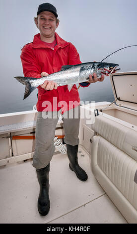 Junger Erwachsener lächelt, auf dem Fischerboot, mit einem gefangenen rosafarbenen Lachs, nebeliger Morgen in der Johnstone Strait vor Vancouver Island, British Columbia, Kanada Stockfoto