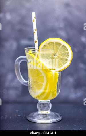 Hausgemachte Limonade in ein Glas mit einem Handgriff über ein grauer Beton Hintergrund. Wasser mit Zitronenscheiben auf einem dunklen Hintergrund Stockfoto