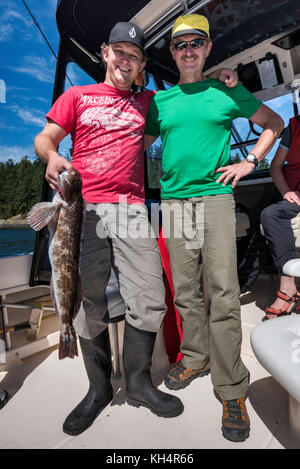 Zwei Männer, Vater und Sohn, mit gefangenem Fisch, Lingcod, auf dem Boot in Vancouver Island, British Columbia, Kanada Stockfoto