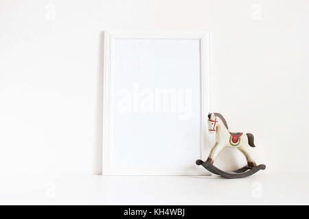 Weiße leere Holzrahmen mockup mit alten hölzernen Pferd Spielzeug auf dem weißen Tisch. styled lieferbar feminine Fotografie. home Decor, Weihnachten Winter Konzept. Stockfoto