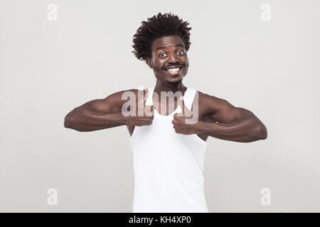 Lustige afro Mann mit Schnurrbart, an der Kamera suchen, lächelnd, Daumen hoch. Studio erschossen. grauer Hintergrund Stockfoto