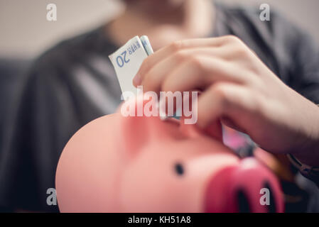 Teenage kaukasischen Jungen setzen 20 euro Hinweis in Sparschwein. Geld sparen. Stockfoto