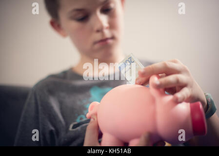 Teenage kaukasischen Jungen setzen 20 euro Hinweis in Sparschwein. Geld sparen. Stockfoto