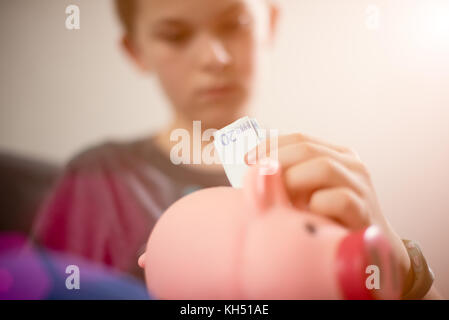 Teenage kaukasischen Jungen setzen 20 euro Hinweis in Sparschwein. Geld sparen. Stockfoto