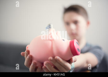 Teenage kaukasischen Jungen setzen 20 euro Hinweis in Sparschwein. Geld sparen. Stockfoto