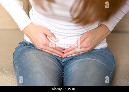 Junge Frau mit Bauchschmerzen beim Sitzen auf der Couch zu Hause Stockfoto