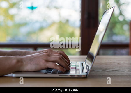 Texteingabe auf einem Laptop vor Fenster auf hölzernen Tisch Stockfoto