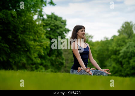 Schöne junge passende Frau Meditation, Atmung, Sitzen mit gekreuzten Beinen im Lotus Haltung im Park im Sommer Tag. Stockfoto