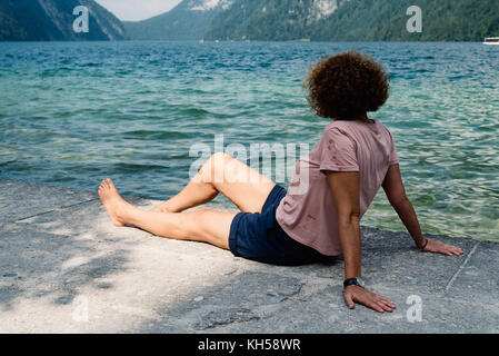 Frau mittleren Alters mit lockigem Haar sitzen am See Stockfoto