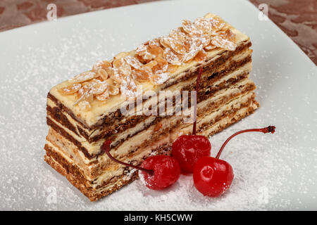 Protein-Mutter Kuchen mit Buttercreme und Kirschen auf einem weißen Teller bestreut mit Puderzucker. close-up Stockfoto