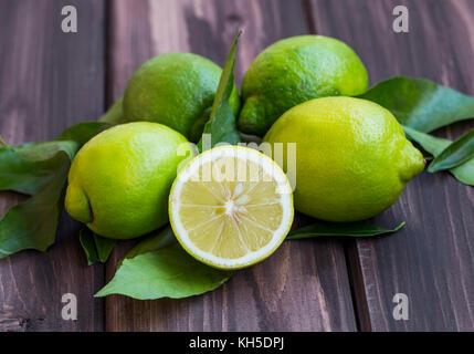 Frische grüne Zitronen, Zitrusfrüchte Heap mit Blättern auf Holzuntergrund Stockfoto
