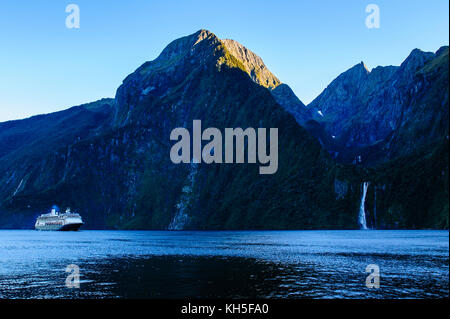 Kreuzfahrtschiff vorbei an einem Wasserfall im Milford Sound, Südinsel, Neuseeland Stockfoto