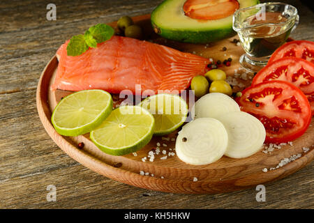 Frisches Gemüse und geräuchertem Fisch auf Holzbrett in rustikale Küche. Lachs, Kalk, Zwiebeln, Oliven, Tomaten und Olivenöl. Konzentrieren Sie sich auf den Vordergrund. Stockfoto