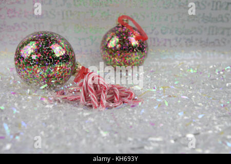 Bunte Weihnachten essen Fotografie Bild der traditionellen Zuckerstange Süßigkeiten in Weiß glänzend Wrap mit hellen Baum deko Kugeln im Hintergrund Stockfoto