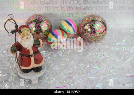 Bunte weihnachten Fotografie Bild der traditionellen Holz- santa claus Ornament in Weiß glänzend Wrap mit hellen Baum deko Kugeln Stockfoto