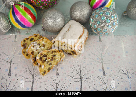 Weihnachten essen Fotografie Bild der traditionellen Obst Stollen mit Baum deko Kugeln in hellen Farben auf glänzenden weißen und hellblauen Hintergrund Stockfoto