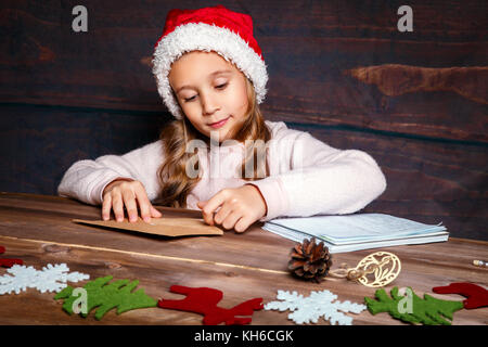 Kind schreibt Brief an Santa Claus. Funny Girl in Santa Hut schreibt Brief an Santa Stockfoto