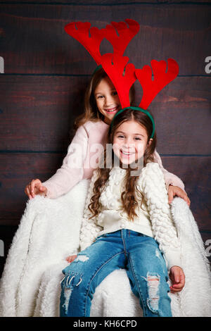 Zwei glückliche kleine lächelnde Mädchen umarmt. Weihnachten Konzept. Lächelnd lustige Schwestern in deer Hörner im Studio. Stockfoto