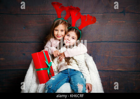 Zwei glückliche kleine lächelnde Mädchen umarmt. Weihnachten Konzept. Lächelnd lustige Schwestern in deer Hörner im Studio. Stockfoto