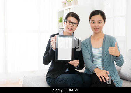 Lächelnd ziemlich Business woman holding mobile digital Tablet mit leerer Bildschirm und Schönheit elegante Mädchen Daumen, die Geste auf Kamera schaut. Stockfoto