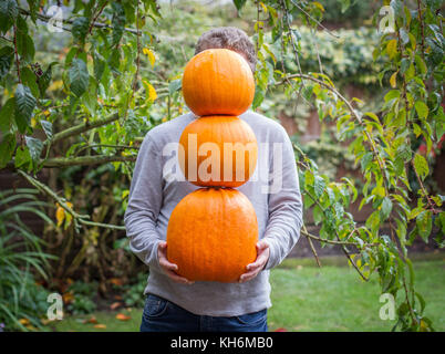 Ein anonymer junger Mann Holding und Ausgleich drei Kürbisse in seine Hände, bedeckte sein Gesicht sind in einem freien Garten. Stockfoto