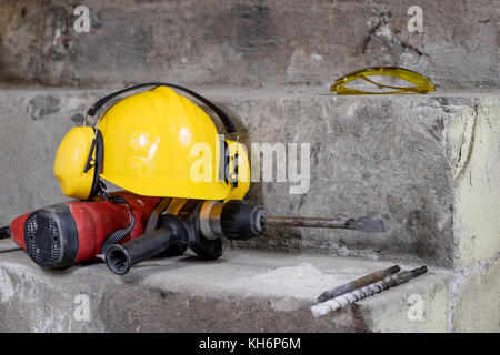 Abriss von Wänden. Elektrische hammer Helm und Gehörschutz liegen auf den Trümmern. alte Ziegel und renovierten Gebäude Wand. Grunzen auf dem Hintergrund Stockfoto