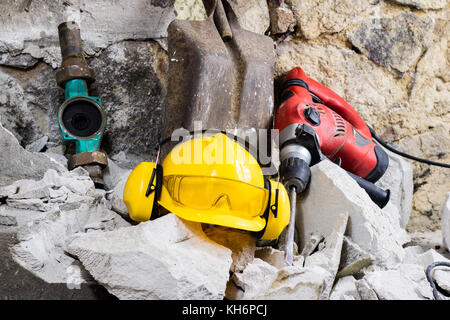 Abriss von Wänden. Elektrische hammer Helm und Gehörschutz liegen auf den Trümmern. alte Ziegel und renovierten Gebäude Wand. Grunzen auf dem Hintergrund Stockfoto