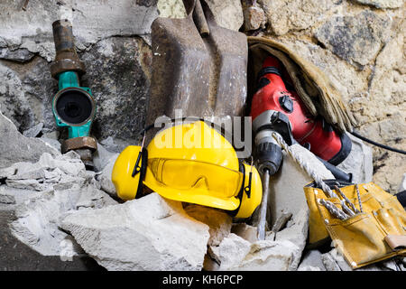 Abriss von Wänden. Elektrische hammer Helm und Gehörschutz liegen auf den Trümmern. alte Ziegel und renovierten Gebäude Wand. Grunzen auf dem Hintergrund Stockfoto