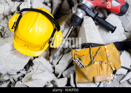 Abriss von Wänden. Elektrische hammer Helm und Gehörschutz liegen auf den Trümmern. alte Ziegel und renovierten Gebäude Wand. Grunzen auf dem Hintergrund Stockfoto