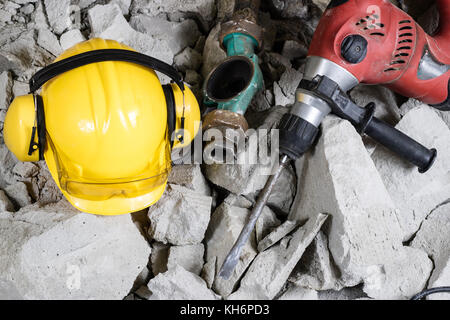 Abriss von Wänden. Elektrische hammer Helm und Gehörschutz liegen auf den Trümmern. alte Ziegel und renovierten Gebäude Wand. Grunzen auf dem Hintergrund Stockfoto