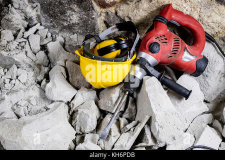 Abriss von Wänden. Elektrische hammer Helm und Gehörschutz liegen auf den Trümmern. alte Ziegel und renovierten Gebäude Wand. Grunzen auf dem Hintergrund Stockfoto