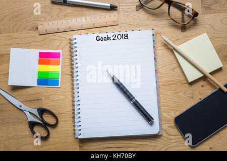 Ein Notizblock mit Zielen für 2018 an der Oberseite und Pen und anderen Accessoires auf einen hölzernen Tisch von oben Stockfoto