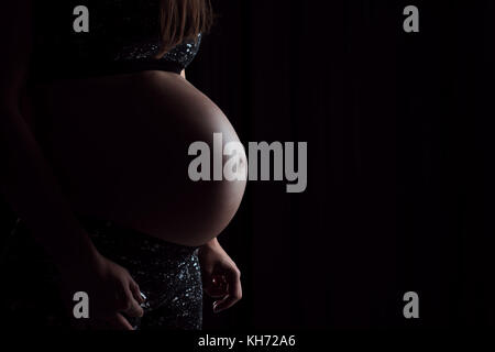 Portrait der schwangeren Frau, ihren Bauch berühren auf schwarzem Hintergrund. Stockfoto