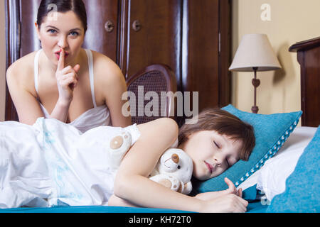 Nahaufnahme, Mutter und Tochter im Schlafzimmer. Mutter mit Raute an Kamera, Tochter geschlossenen Augen und Schlafen. studio Shot Stockfoto