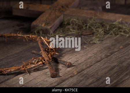 Dornenkrone und Nägel mit einem Kreuz im Hintergrund auf einer hölzernen Oberfläche Stockfoto