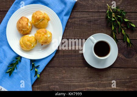 Frisch gebackene Brötchen eclairs, gefüllt mit pikanter Hüttenkäse und eine Tasse Kaffee (Espresso) auf einem dunklen Hintergrund. leichtes Frühstück. die Ansicht von oben Stockfoto