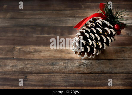 Riesige Pine Cone mit Glitzer verziert, rot Stechpalme Beeren, Tanne, Farbband und Mini LED-Leuchten auf dunkelbraunen Hintergrund mit viel Tempo zu kopieren. Stockfoto