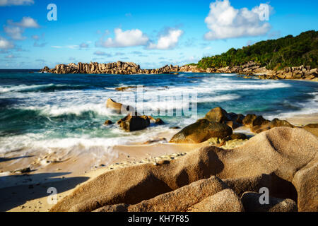 Wellen gegen golden Granitfelsen vor einem Dschungel. rauhe Wildnis - eine andere Seite der Paradies auf den Seychellen. Stockfoto