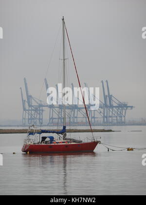 Queenborough, Kent, UK. 15 Nov, 2017. UK Wetter: Eine ruhige und relativ milden November Tag in der historischen Stadt Queenborough auf der Insel Sheppey. Eine Yacht in Queenborough Hafen, mit den Kranichen von Thames Port in der Ferne. Credit: James Bell/Alamy leben Nachrichten Stockfoto