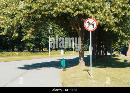 Asphaltierte Straße zwischen den alten grünen Bäumen im Park mit einem Schild verboten, mit den Hunden zu gehen. Hunde nicht erlaubt nicht im Bereich Zeichen erlaubt. Stockfoto