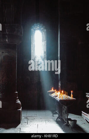 Einen dunklen Hintergrund der alten armenischen christlichen Kirche Kloster Innenraum mit einer Sun Ray fallen auf den Kerzen aus dem Fenster. Abstrakte christliche Religion Stockfoto