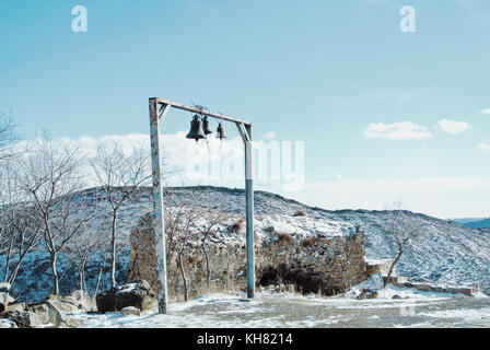 Drei Glocken und die Ruinen einer Mauer in der Nähe des dschuari orthodoxe Kloster in der Nähe von mzcheta, Ost Georgien, im Winter bewölkten Tag. mountaiins abgedeckt w Stockfoto