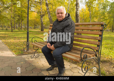 Der einsame Grauhaariger alter Mann, ruht auf einer Holzbank in einem Park an einem sonnigen Herbsttag. Stockfoto