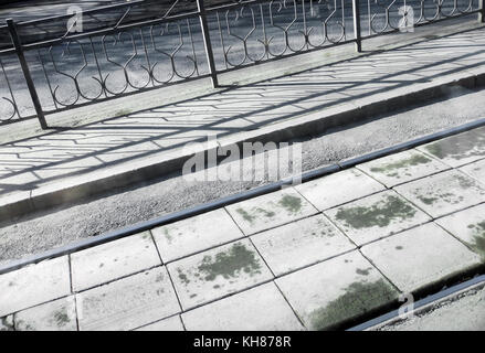 Diagonal geschossen. Straßenbahn, Gehweg, Zaun und Schattierungen in sonnigen Morgen. Stockfoto