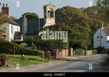 Blick auf ruhigen, ländlichen Feldweg in Richtung hohen Glockenturm der Kirche St. Giles & attraktive Dorf Hütten - Burnby, East Yorkshire, England, UK. Stockfoto