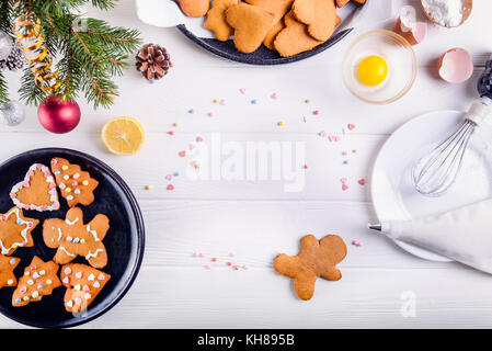 Weihnachten hausgemachte Lebkuchen Cookies auf die weiße Holztisch, Weihnachten Hintergrund Konzept. Der Prozess der Verzierung mit Baiser Sahne. Selektive konzentrieren. Platz für Text, Ansicht von oben Stockfoto