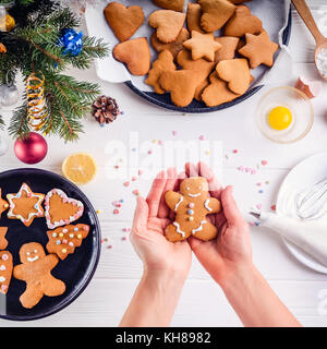 Frau Hände, die traditionellen christmas gingerbread man Cookies. Weiße Holztisch mit ingrediens und Dekoration details. Weihnachten Konzept. Der Prozess der Verzierung mit Baiser Sahne. Stockfoto