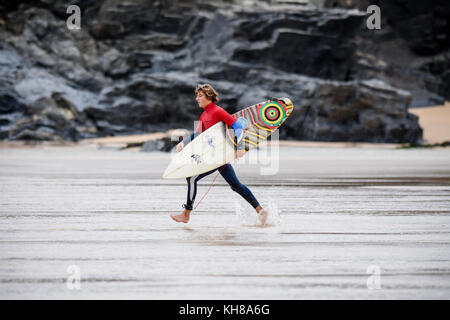 Surfer in Cornwall, England, der ebach mit seinem Surfboard unter dem Arm Stockfoto