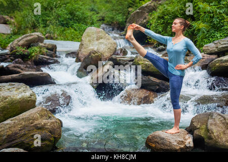 Frau tut Ashtanga Vinyasa Yoga Asana im Freien am Wasserfall Stockfoto