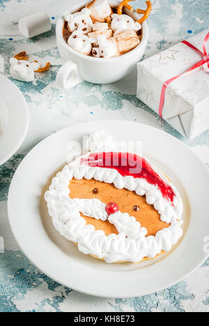 Idee für Kinder Weihnachten Frühstück: Pfannkuchen wie Santa Claus und Rotwild eingerichtet, Kakao mit Teddybären und Rotwild Marshmallow. Auf einem Hellblau Stockfoto